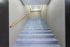 A staircase with a handrail, marble steps, and a modern light fixture at the top. - Huamin Hotel (Huashan Hospital Hotel Jiangsu Road Shanghai) (Shanghai)