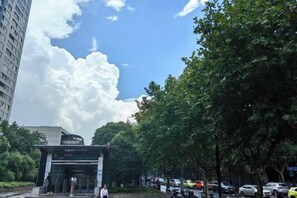 A street view with a building entrance, trees, and parked cars. - Huamin Hotel (Huashan Hospital Hotel Jiangsu Road Shanghai) (Shanghai)