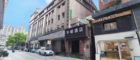 A hotel with a signboard, a visible entrance, and a street view with parked cars and buildings.