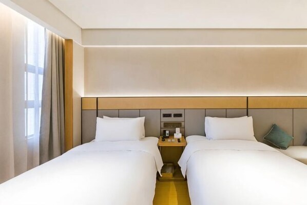 A hotel room with two beds, a nightstand, and a view of the city.