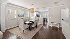 A dining area with a wooden table and chairs, a hanging light fixture, and a view into the kitchen. - Charming Uptown Charlotte Oasis with En Suites & Balcony with quiet street, walk to coffee shops nearby and minutes to convention center and uptown offices. (Charlotte)