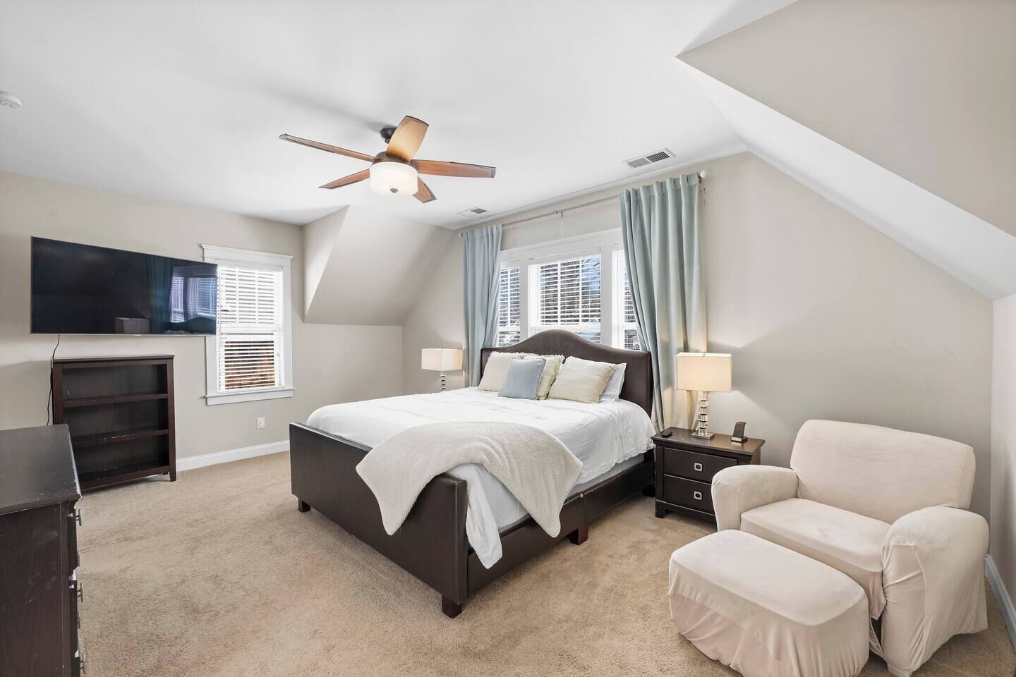 A bedroom with a large bed, a ceiling fan, a TV, a desk, and a chair.