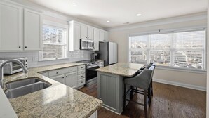A modern kitchen with white cabinets, granite countertops, a built-in oven, and a large window with blinds. - Charming Uptown Charlotte Oasis with En Suites & Balcony with quiet street, walk to coffee shops nearby and minutes to convention center and uptown offices. (Charlotte)