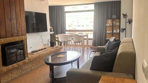 A living room with a fireplace, a TV mounted on the wall, a dining area with a table and chairs, and a sofa.