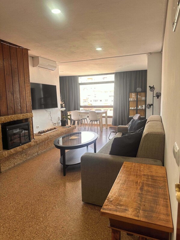 Ein Wohnzimmer mit Kamin, Wand-Fernseher, Essbereich mit Tisch und Stühlen sowie einer Couch.