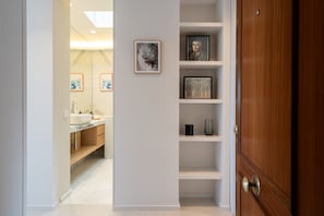 A hallway with a wooden door, a white wall with framed artwork, and a bathroom with a sink and mirror. - atico con terraza en el centro de alquiler temporal (Madrid)