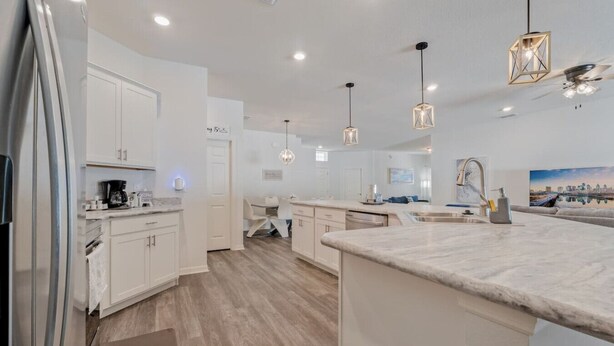 Una cocina moderna con armarios blancos, encimera de mármol e iluminación colgante.