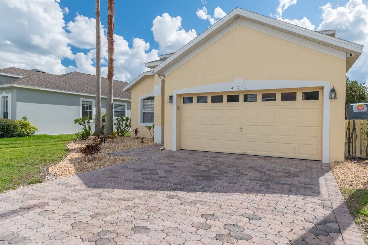 Une maison de plain-pied avec une porte de garage beige, une allée pavée et une pelouse bien entretenue.