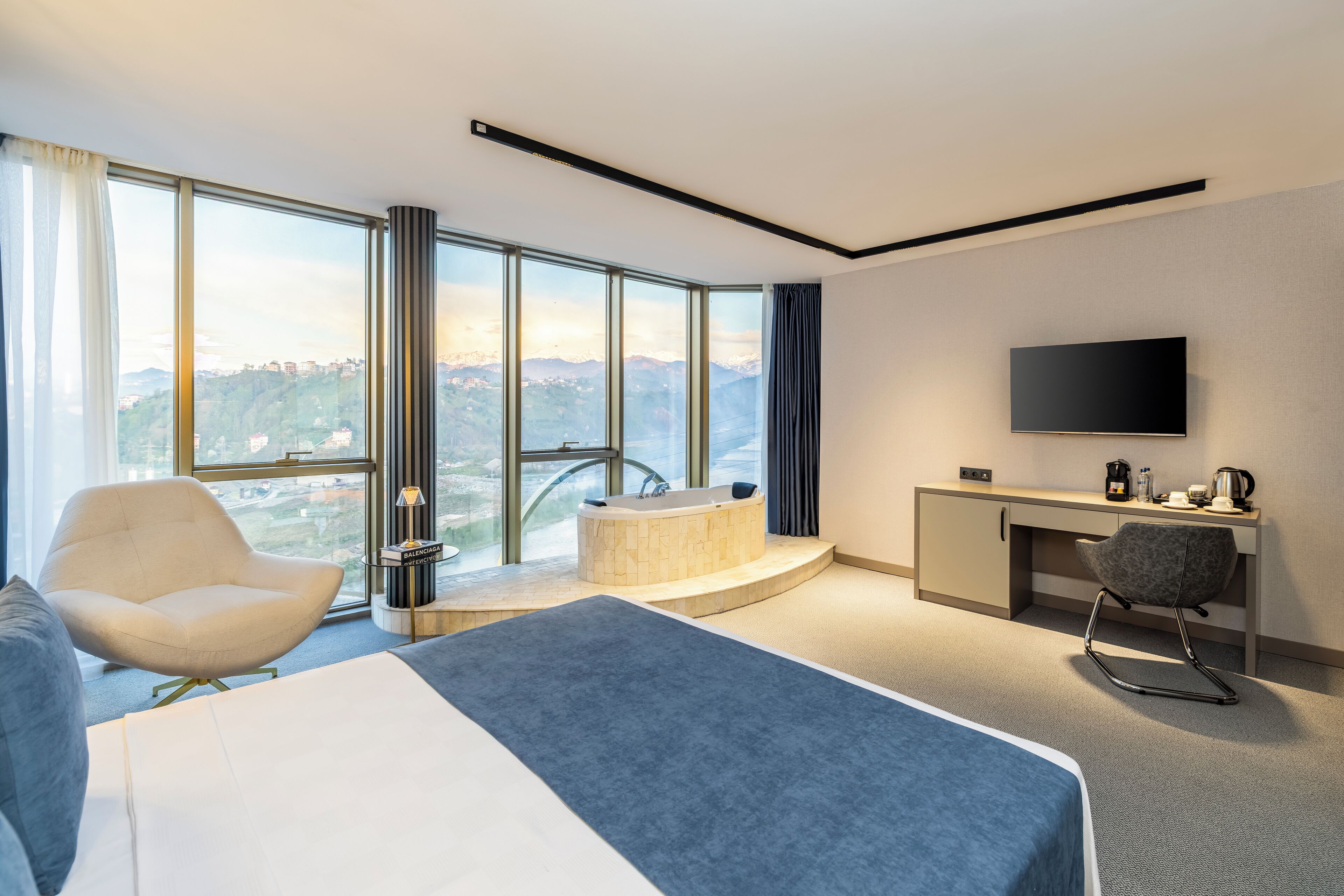 Ett modernt hotellrum med en stor säng, en sittgrupp med en fåtölj, ett skrivbord, en platt-TV och ett badkar.