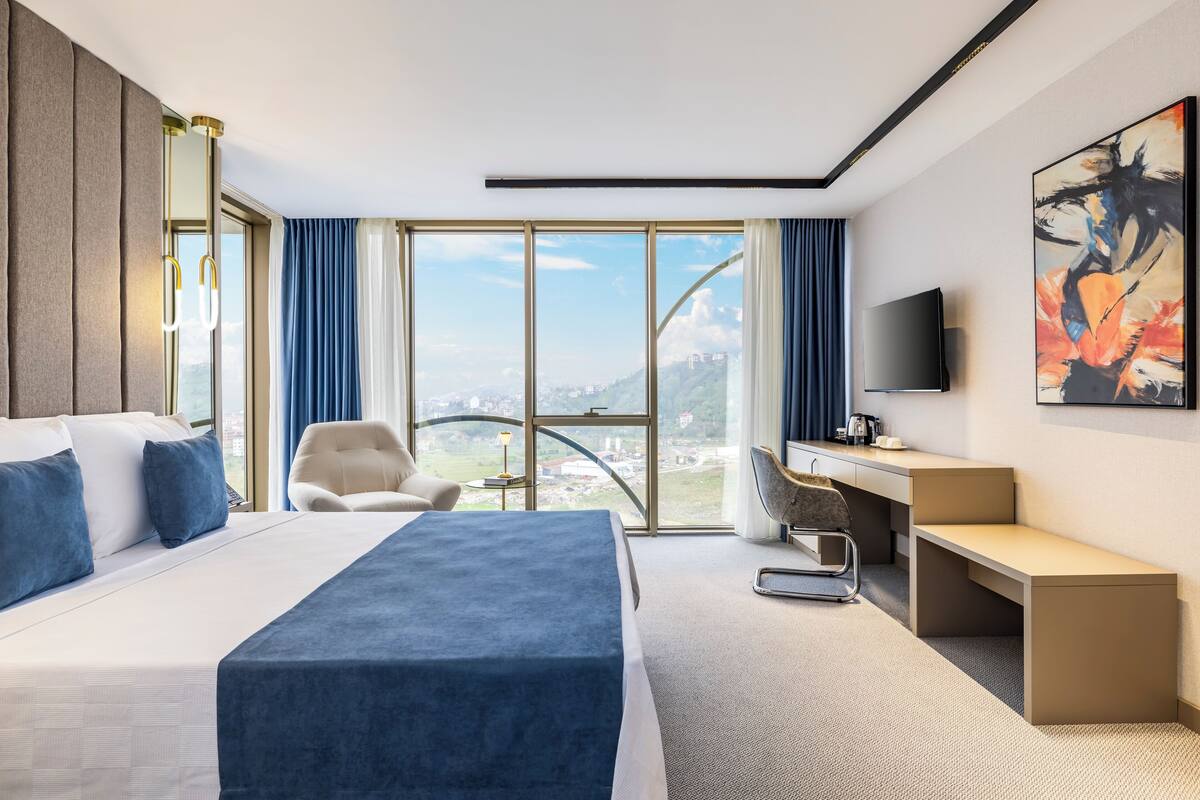 Ett modernt hotellrum med en stor säng, ett skrivbord, en stol och en TV.