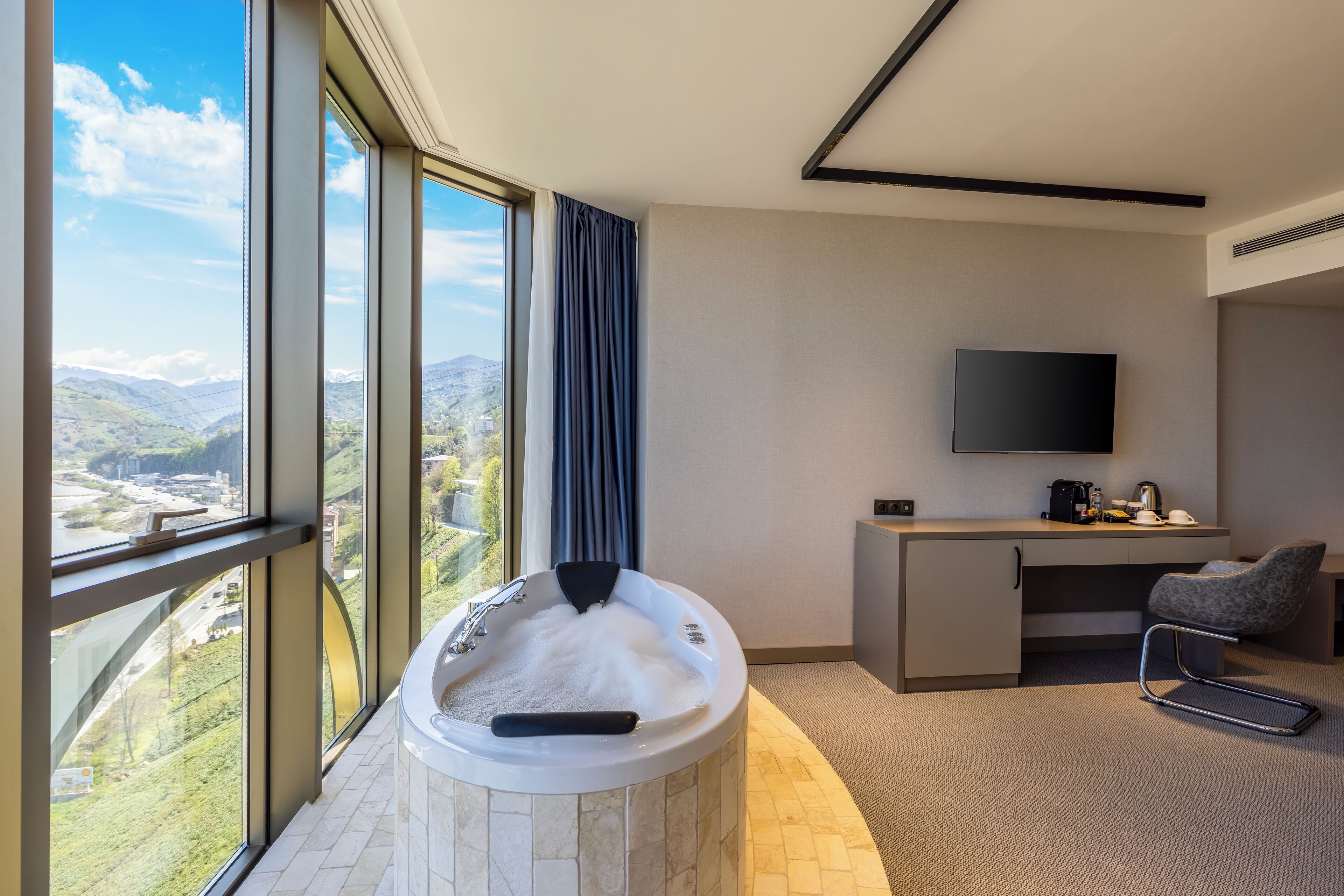 Una habitación de hotel moderna con un ventanal grande que ofrece una vista panorámica de montañas y una ciudad.