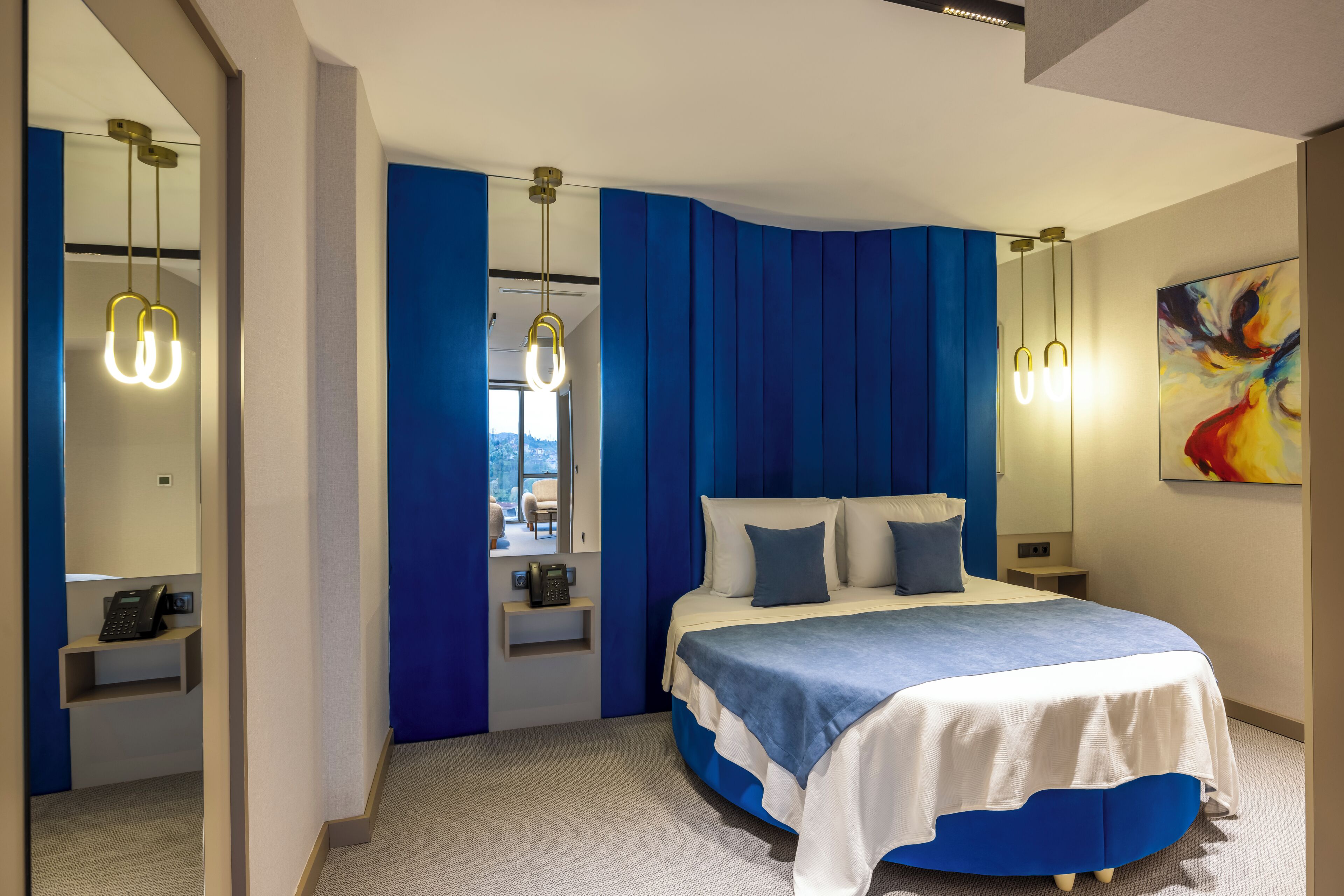 Un dormitorio moderno con una cama curvada, paredes de acento azul e iluminación colgante.