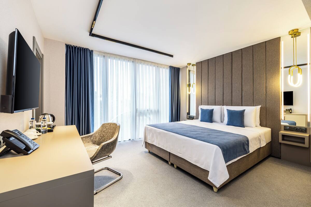 Ett modernt hotellrum med en stor säng, ett skrivbord med en telefon, en stol och en tv.