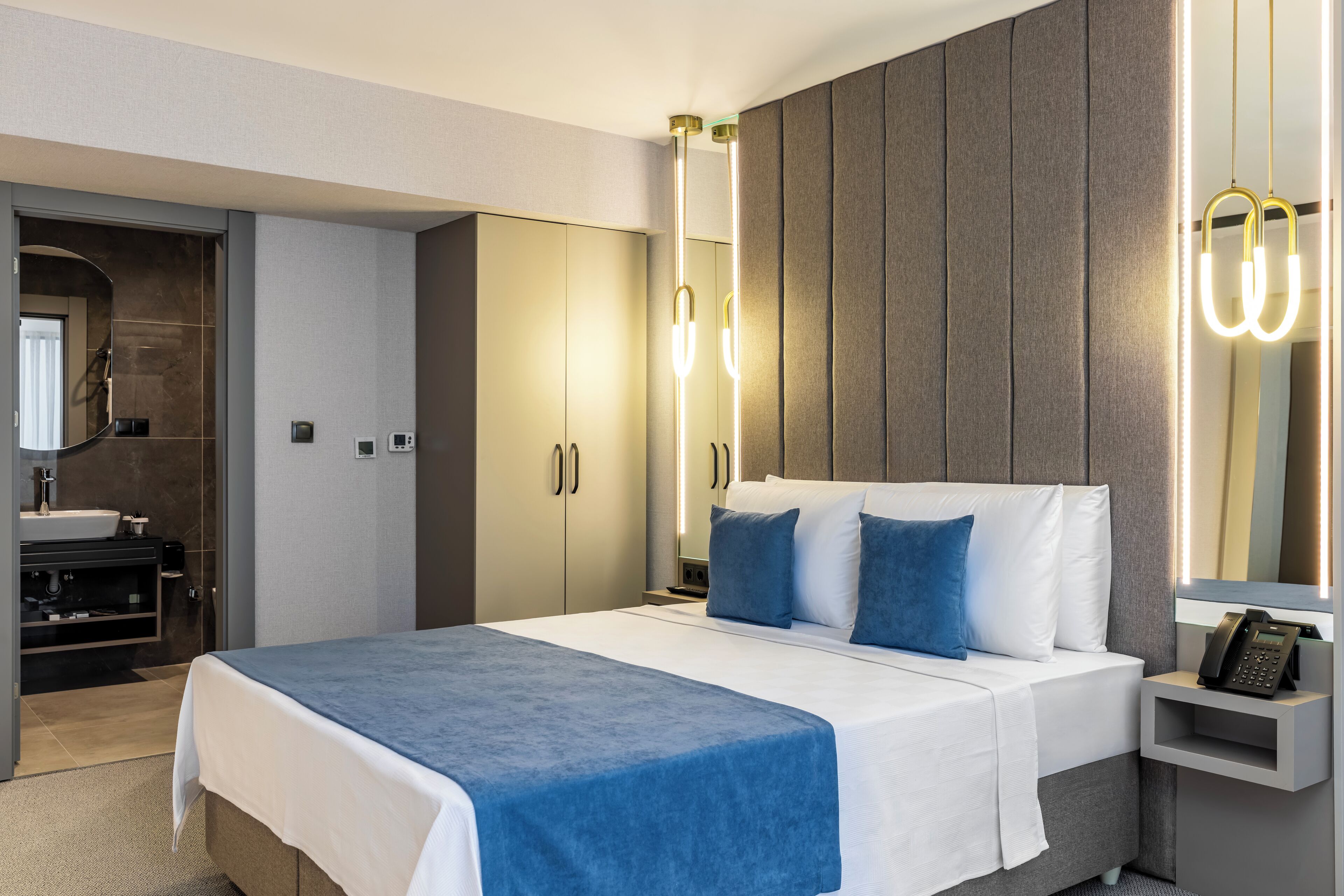 A modern hotel room with a large bed, bedside table, and a built-in wardrobe.