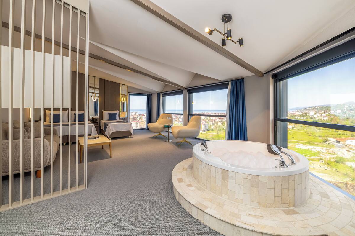 Ett modernt hotellrum med ett stort fönster, ett badkar, en soffa och ett skrivbord.