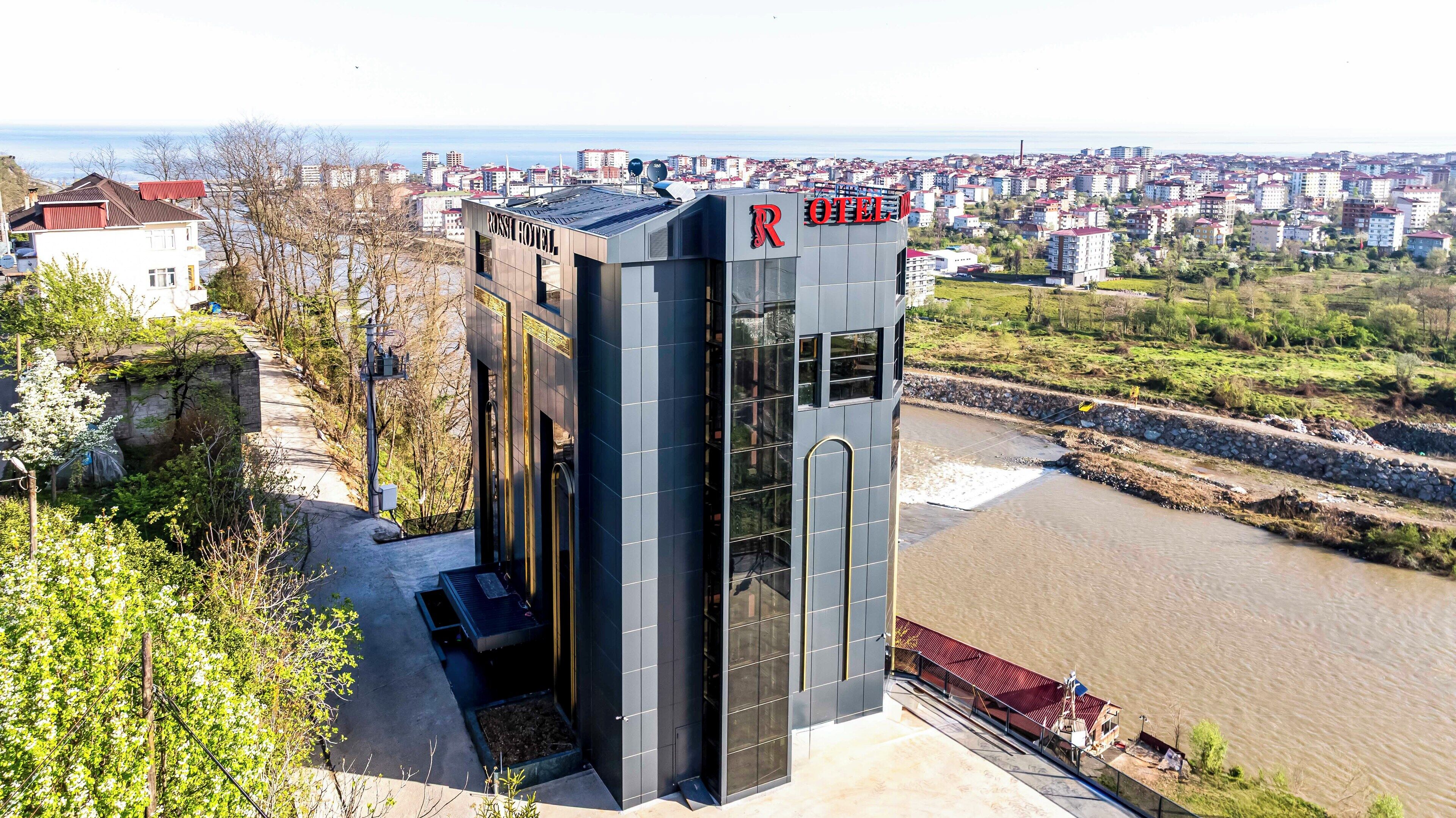 Un bâtiment moderne avec une enseigne indiquant « ROSSI HOTEL », et en arrière-plan, une vue sur une rivière et le paysage urbain.