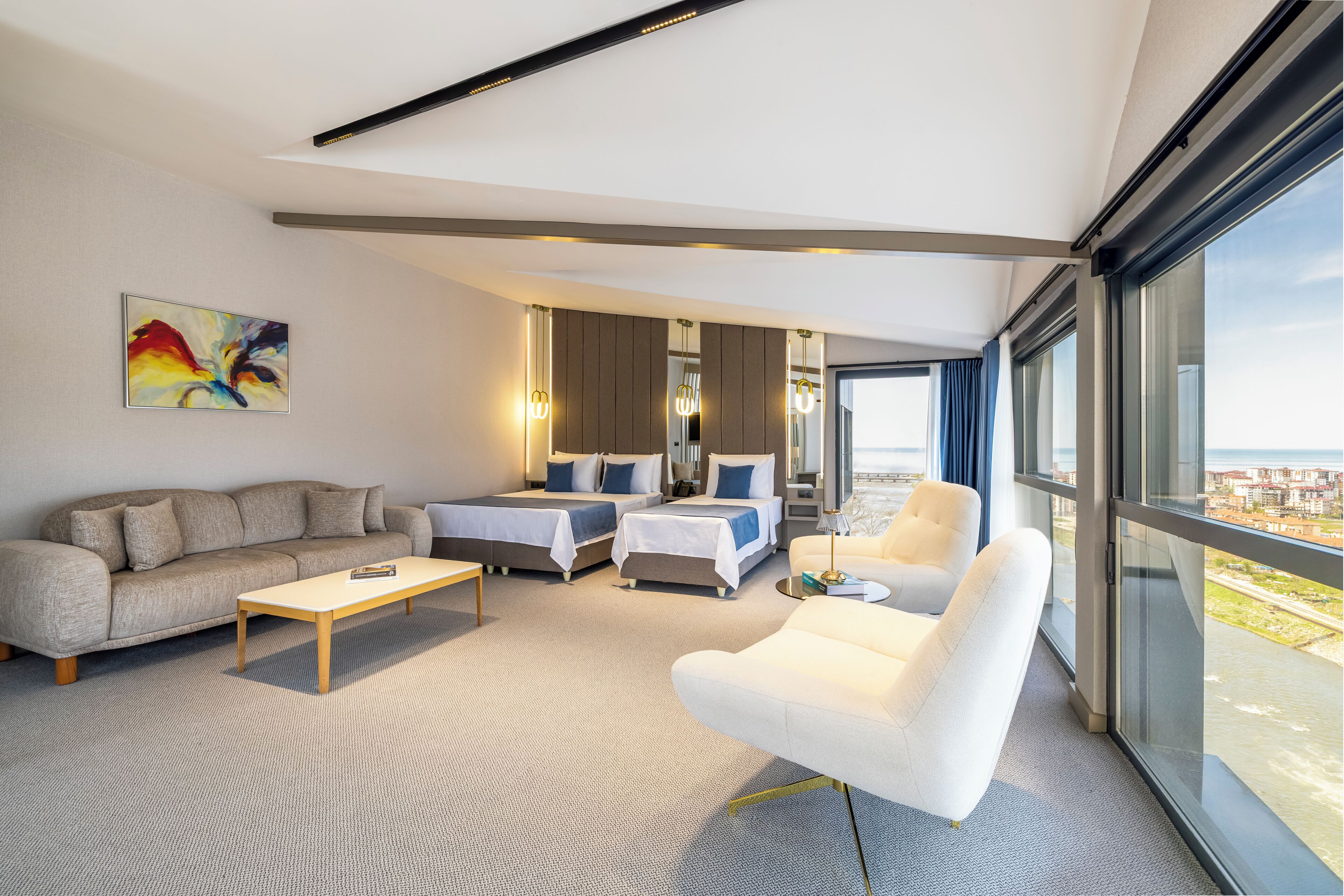 Une chambre d’hôtel moderne, dotée d’un canapé, de deux lits, d’une table basse et offrant une vue sur le paysage urbain grâce à de grandes fenêtres.