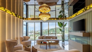 A spacious living room with a large window, a chandelier, and a flat-screen TV. - Rossi Luxury Hotel (Ardesen)