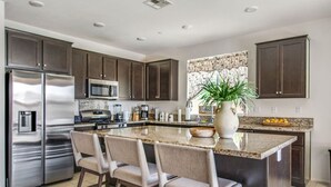 Une cuisine moderne avec des meubles en bois foncé, des appareils en acier inoxydable, un plan de travail en granit et un îlot central doté de tabourets de bar.