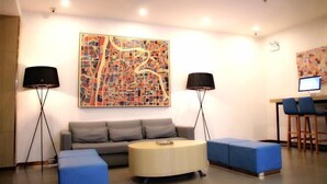 A modern living room with a grey sofa, a round coffee table, and blue ottomans. There are two floor lamps and a large abstract painting on the wall. - Tianyue Hotel (Shangqiu Ancient City First People's Hospital) (Shangqiu)