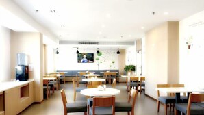 A modern restaurant with round tables and chairs, a counter with a coffee machine, and a wall-mounted TV. - Tianyue Hotel (Shangqiu Ancient City First People's Hospital) (Shangqiu)