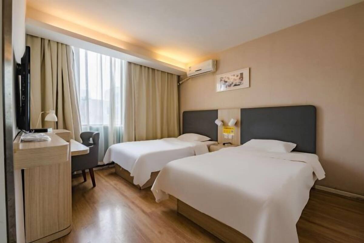 Quarto de hotel com duas camas, uma escrivaninha, uma cadeira, uma televisão e uma janela com cortinas.