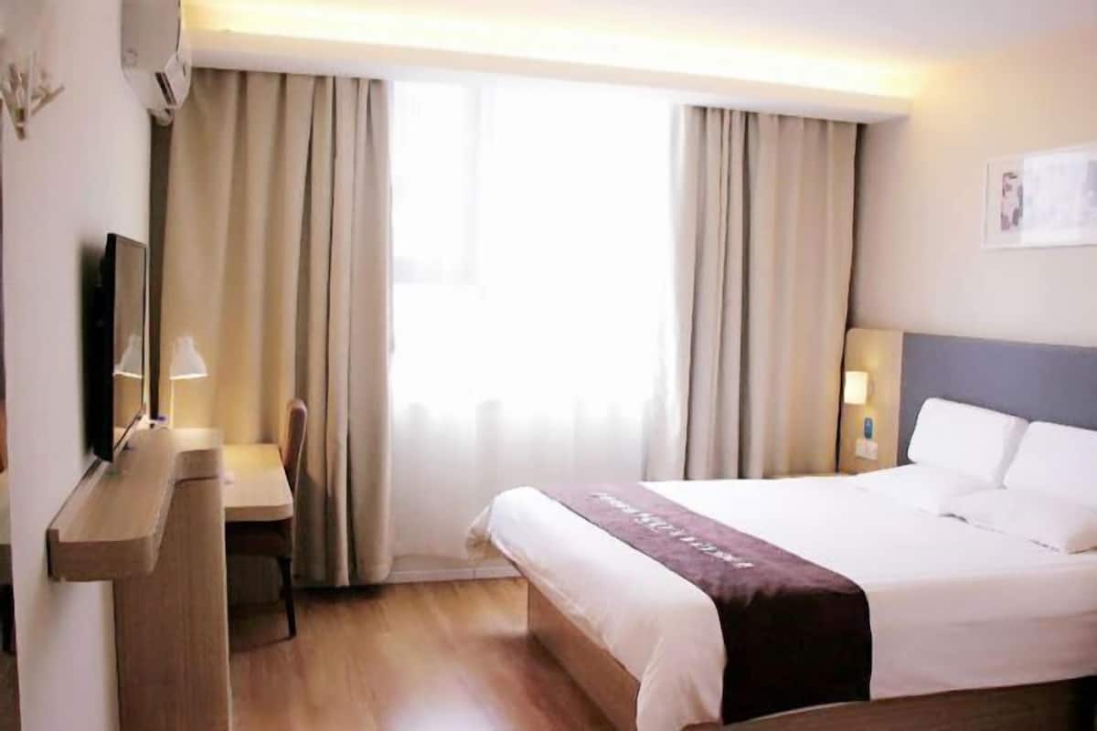 Quarto de hotel com cama, escrivaninha, cadeira, televisão e janela com cortinas.