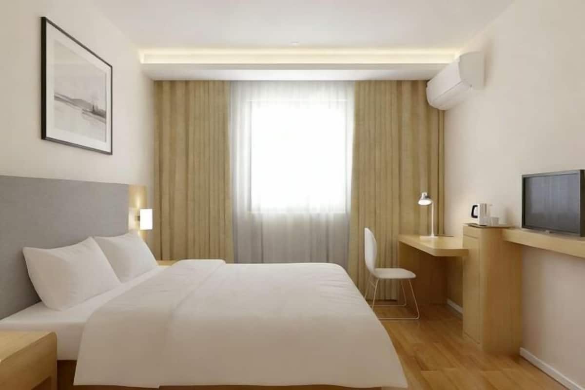 Quarto de hotel com cama, escrivaninha, cadeira, televisão e janela com cortinas.