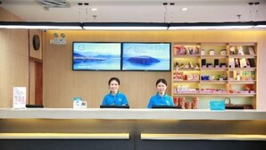 A reception desk with two staff members, a television screen, and shelves with various items. - Tianyue Hotel (Shangqiu Ancient City First People's Hospital) (Shangqiu)
