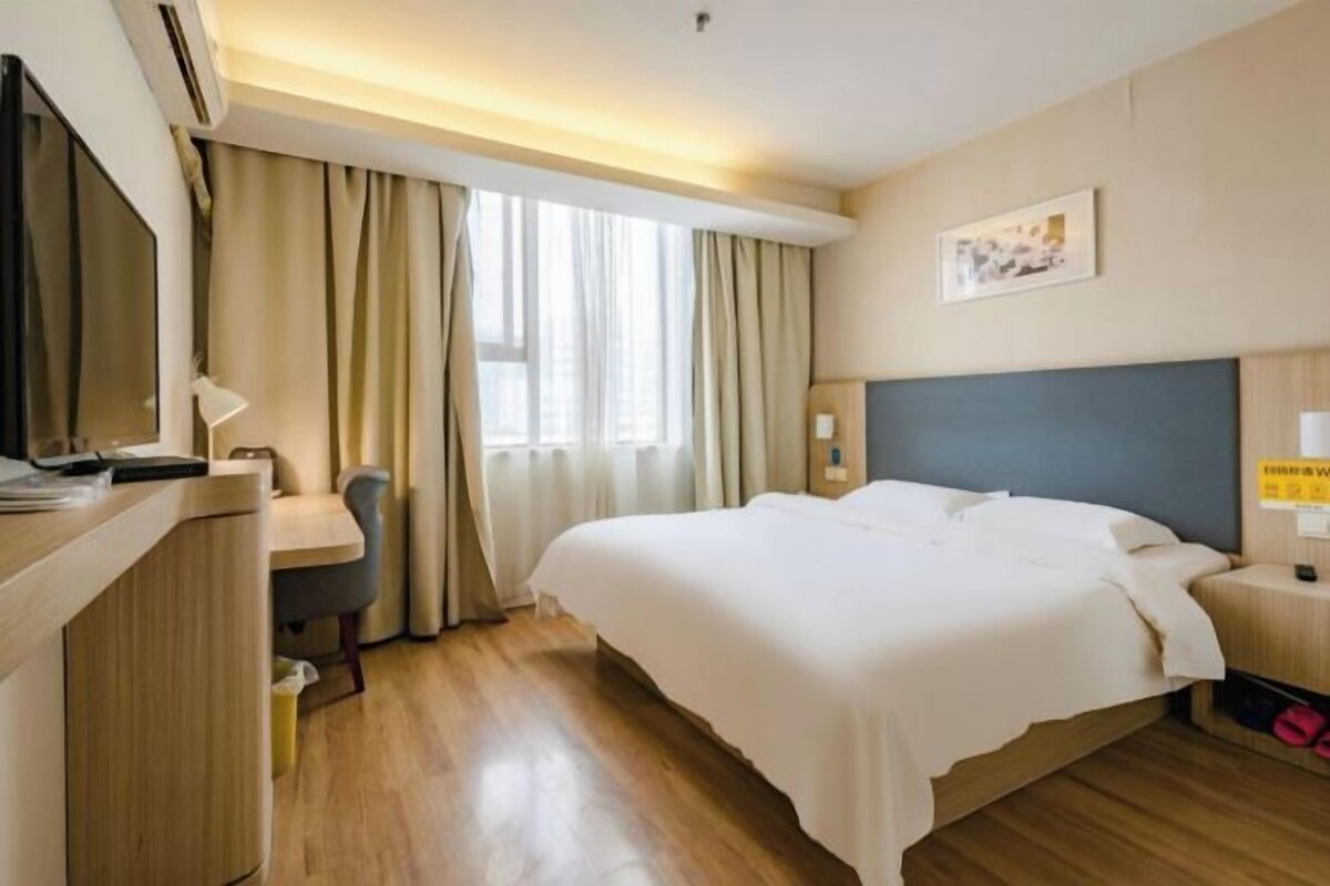 A hotel room with a bed, a desk, a chair, and a television.