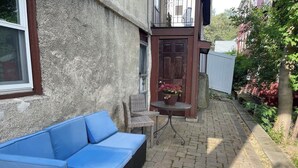 Un cortile con un divano blu, mobili in vimini e un tavolino con un vaso di fiori.
