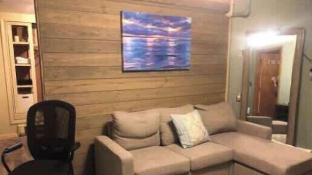 Un soggiorno angolare con un divano componibile beige, una sedia da ufficio nera e una parete in legno con un quadro.