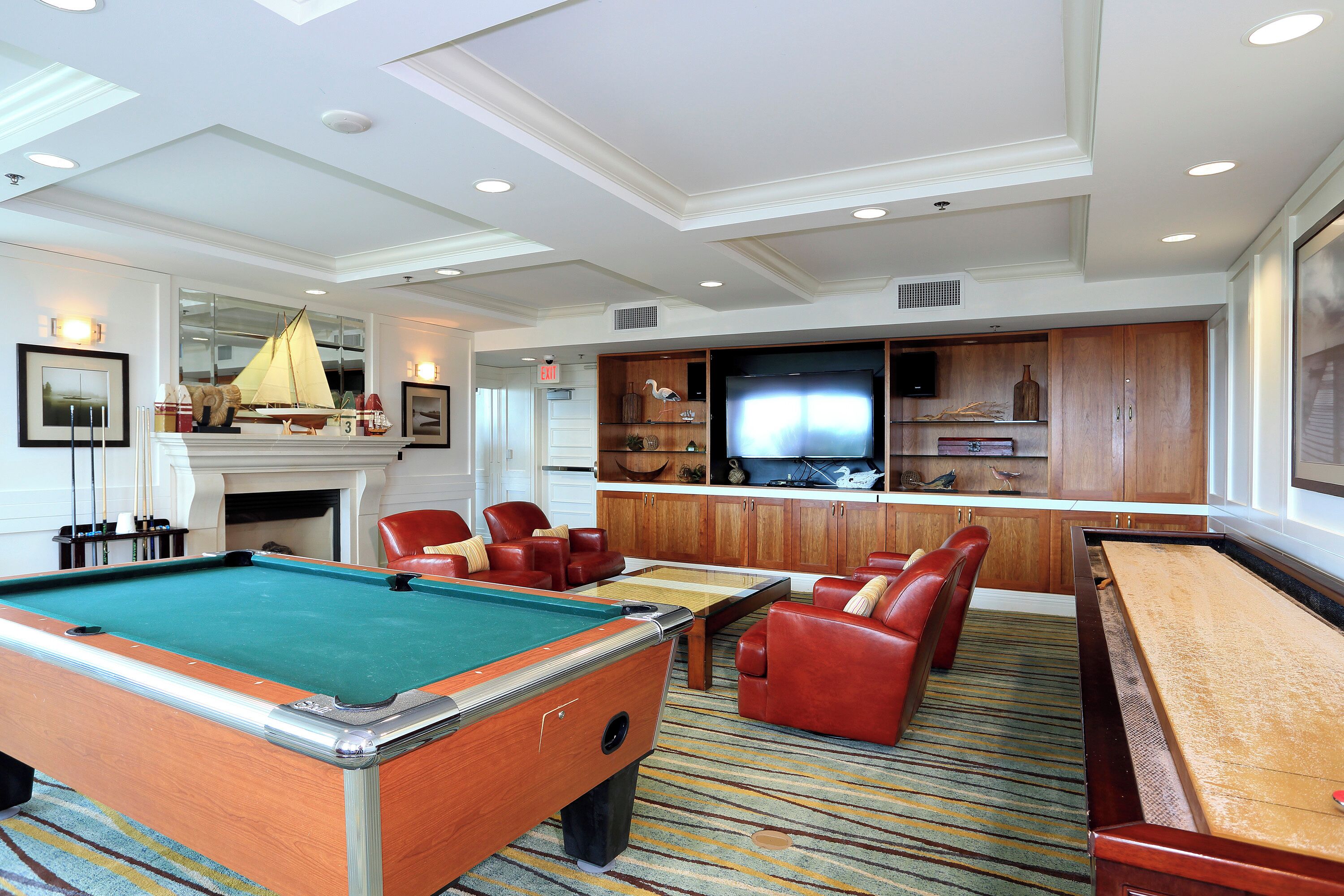 A pool table, red leather chairs, a bar, and a television in a well-lit room with wooden cabinets and a fireplace.