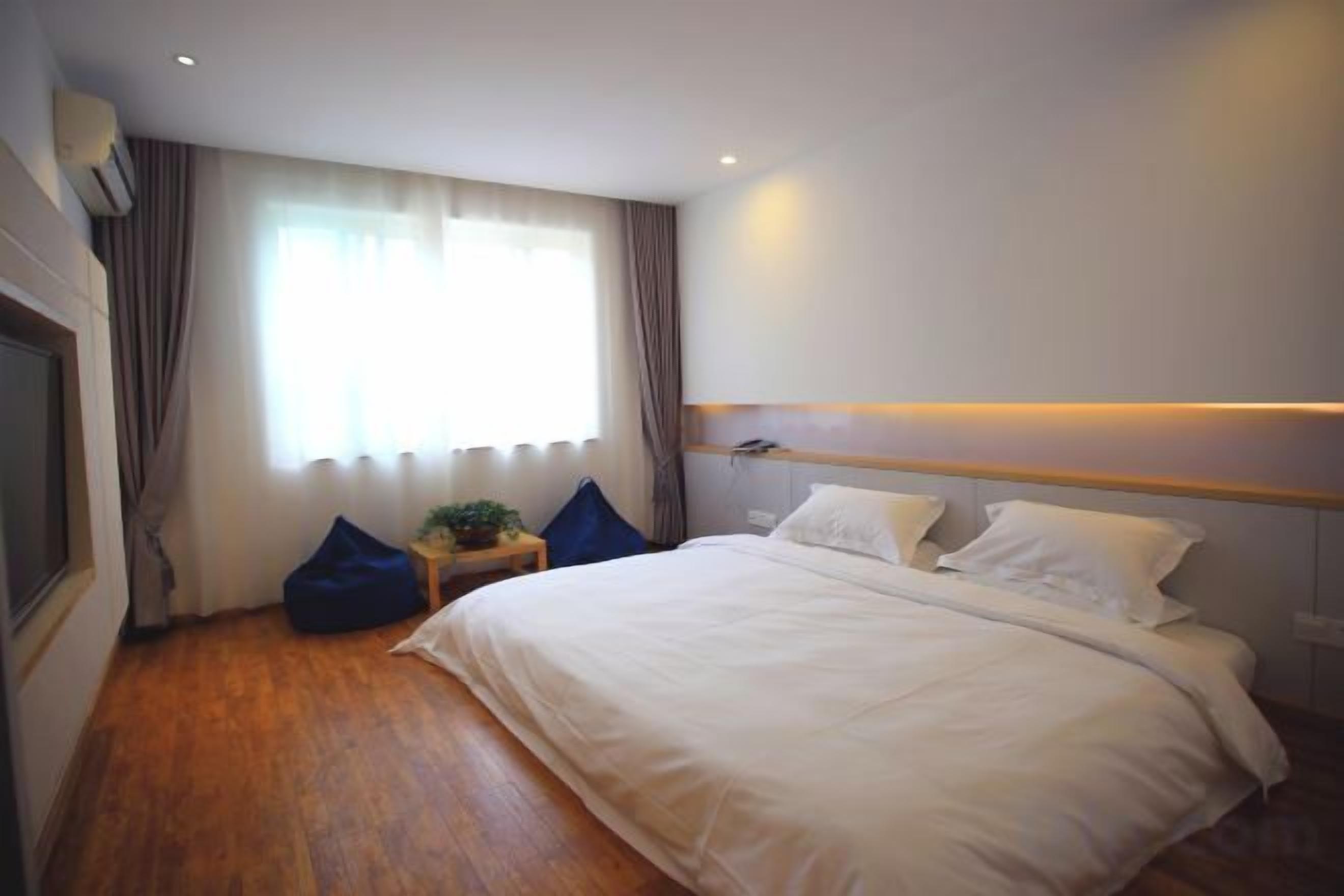 Een hotelkamer met een bed, nachtkastje, raam met gordijnen en een houten vloer.
