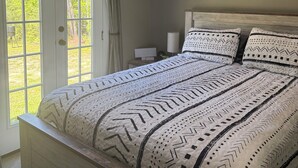 Un dormitorio con cama, ventilador de techo, mesita de noche y ventana con cortinas.