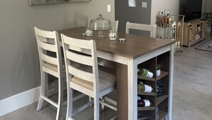 Un comedor con una mesa de madera, cuatro sillas, un cuadro de flores y un televisor al fondo.