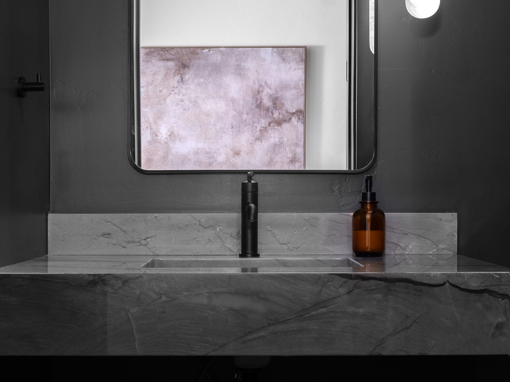 A bathroom with a marble countertop, a black faucet, and a bottle of liquid soap.