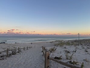 A sandy beach with a wooden fence leading to the water, a wooden boardwalk, and a clear sky.