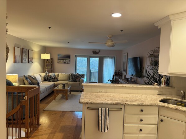 A spacious living area with a sofa, coffee table, and a dining table. There is a kitchen with white cabinets and a granite countertop.