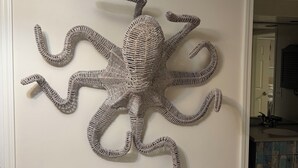 Une sculpture d’un poulpe, fixée au mur, se trouve dans une pièce où il y a une table blanche et une porte qui mène à une autre pièce.