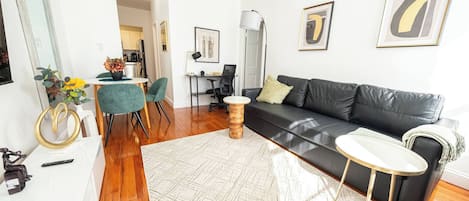 Un salon moderne avec un canapé en cuir noir, une table basse ronde et un coin repas comprenant une chaise verte et une petite table.
