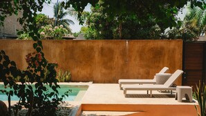 A pool area with lounge chairs, a concrete wall, and tropical plants. - Maralagua (Puerto Escondido)