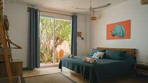 A bedroom with a bed, a ceiling fan, a view of greenery outside, and a painting on the wall. - Maralagua (Puerto Escondido)