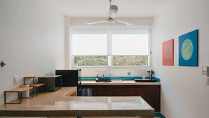A compact kitchen with a window, a ceiling fan, and a dining area with two chairs. - Maralagua (Puerto Escondido)