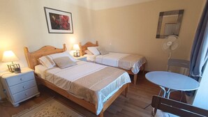 Ein Zimmer mit zwei Holzbett, einem kleinen Tisch, einem Stuhl, einem Nachttisch mit Lampe und einem Spiegel an der Wand.