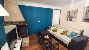 Ein Wohnzimmer mit blauer Akzentwand, einer Couch mit gemusterten Kissen, einem Glastisch und einem Kamin.
