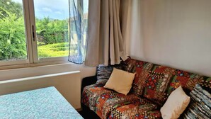 Une chambre avec un lit, une fenêtre avec des rideaux et une vue sur la verdure.