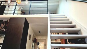 Un escalier doté d’une rampe métallique et d’une balustrade en bois, menant à un niveau inférieur avec un plancher en bois foncé et une bibliothèque.