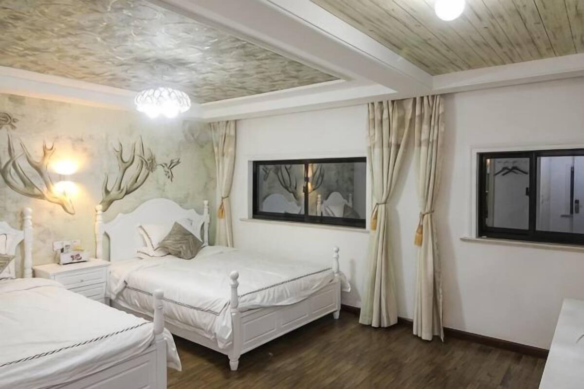 Quarto com duas camas brancas, teto com painéis de madeira e arte na parede com chifres.