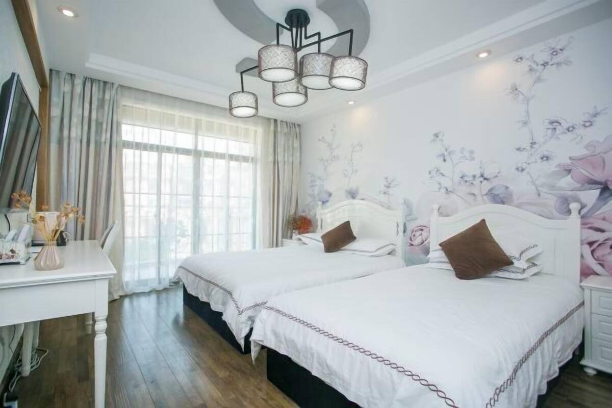 Quarto com duas camas, uma escrivaninha, um candelabro e um mural floral.